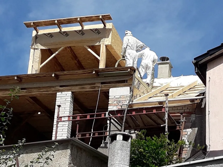 Pracovníci stříkají izolaci na dřevěnou konstrukci střešní nástavby nad okolními střechami