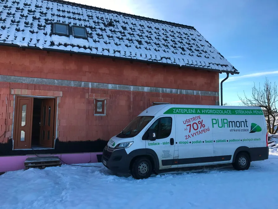 Dodávka PURmont zaparkovaná u zasněžené cihlové novostavby s hotovou střechou